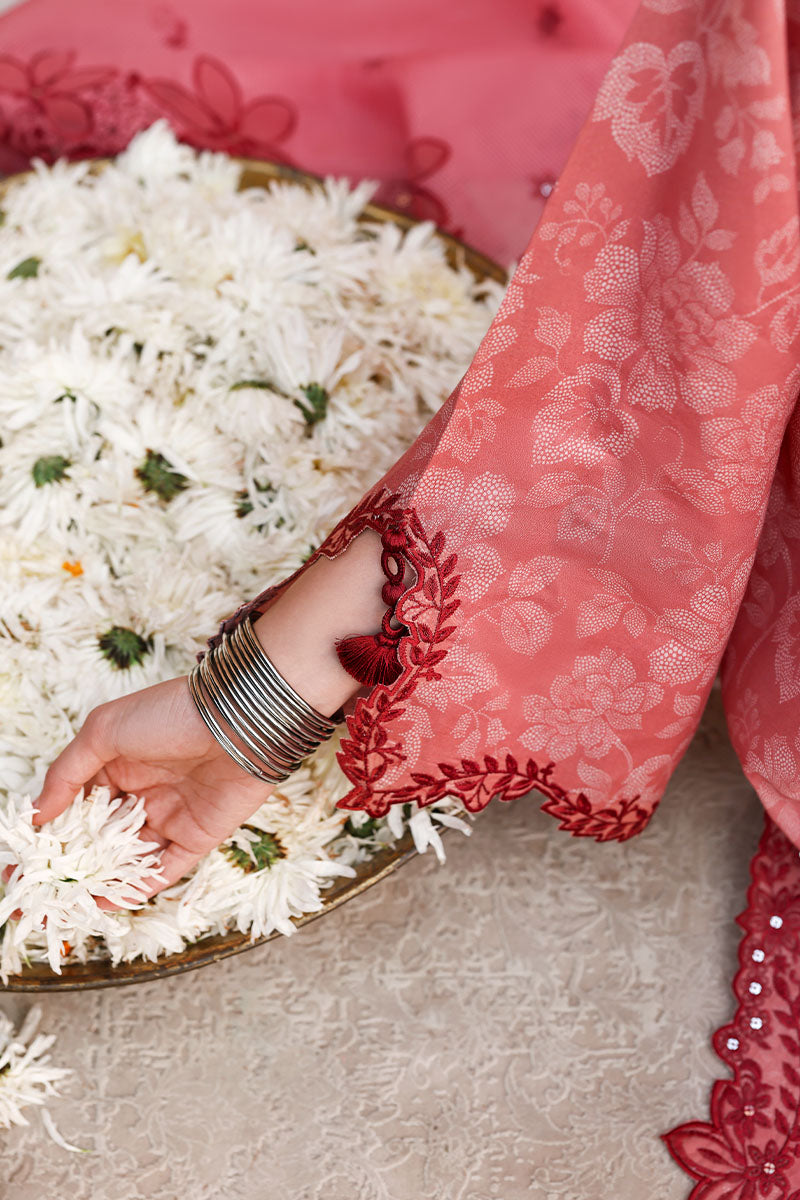 Close-up of embroidered sleeve details showing floral tassels on the soft pink lawn fabric beside white flowers in a brass bowl.
