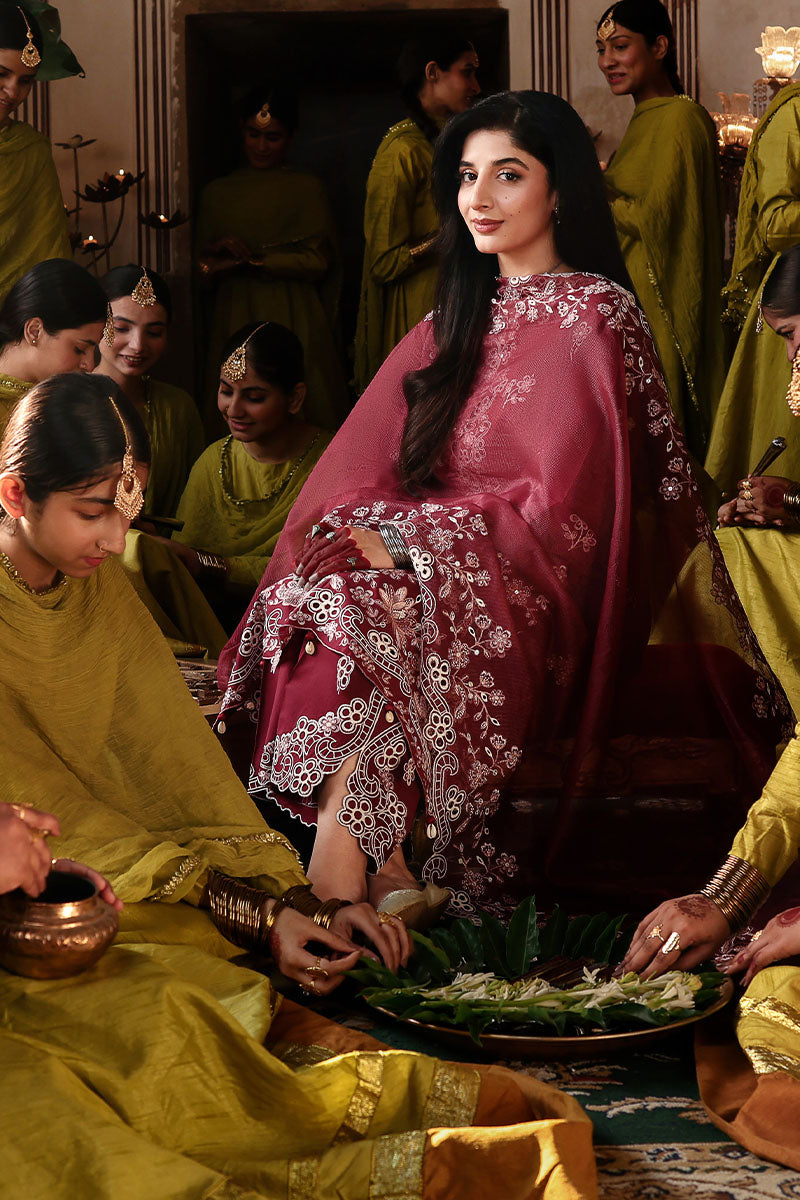 Woman sitting with embroidered crimson lawn suit draped with matching net dupatta, surrounded by women in green formal dresses
