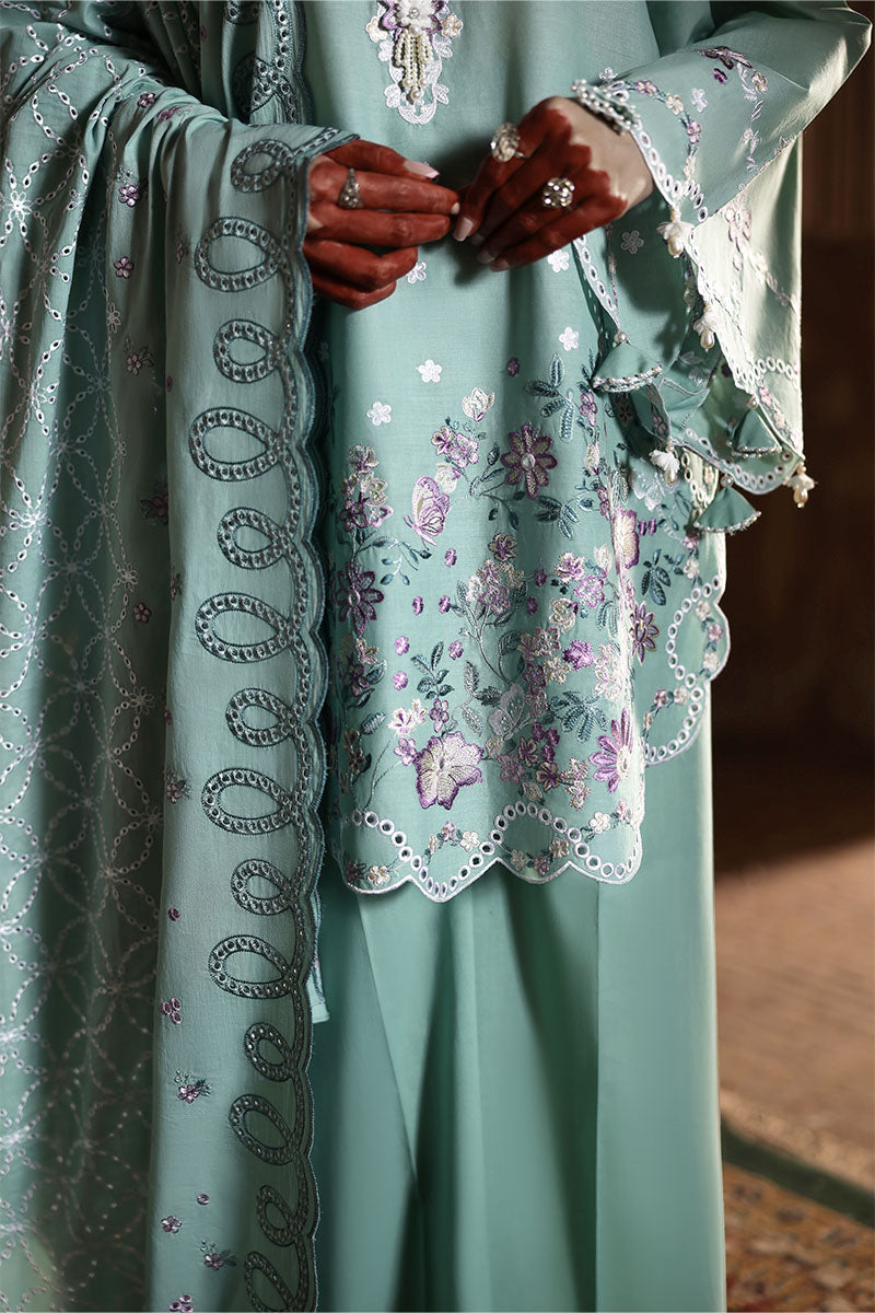 Close-up of hands showing intricate floral embroidery and scalloped edges on the pastel green lawn fabric of the suit.