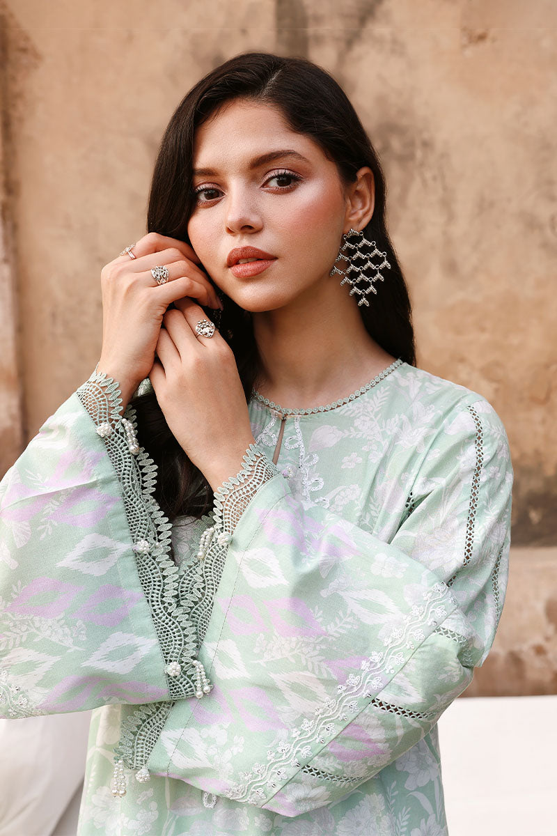 Model showing detailed embroidery and lace inserts on the long sleeves of the sage green floral shirt, wearing statement earrings and rings