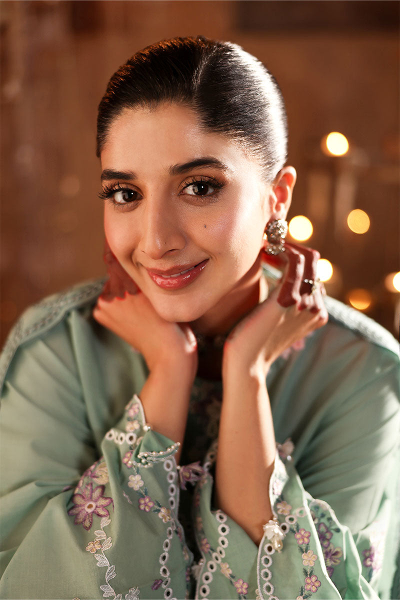 Close-up portrait of a woman smiling, wearing silver jewelry and pastel green embroidered lawn suit with detailed sleeve embroidery.