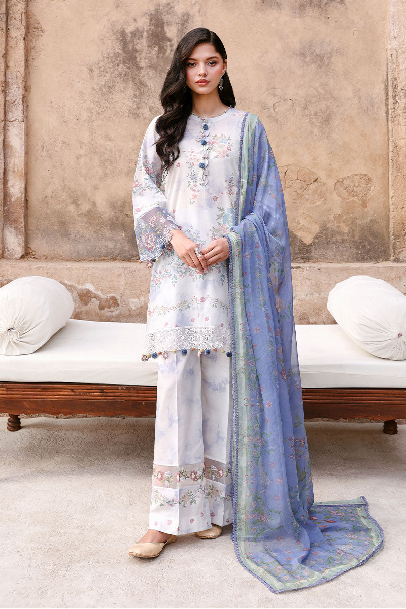 Woman modeling Vintage Petal 3-piece lawn suit standing against rustic wall with floral print shirt, wide pants, and blue chiffon dupatta