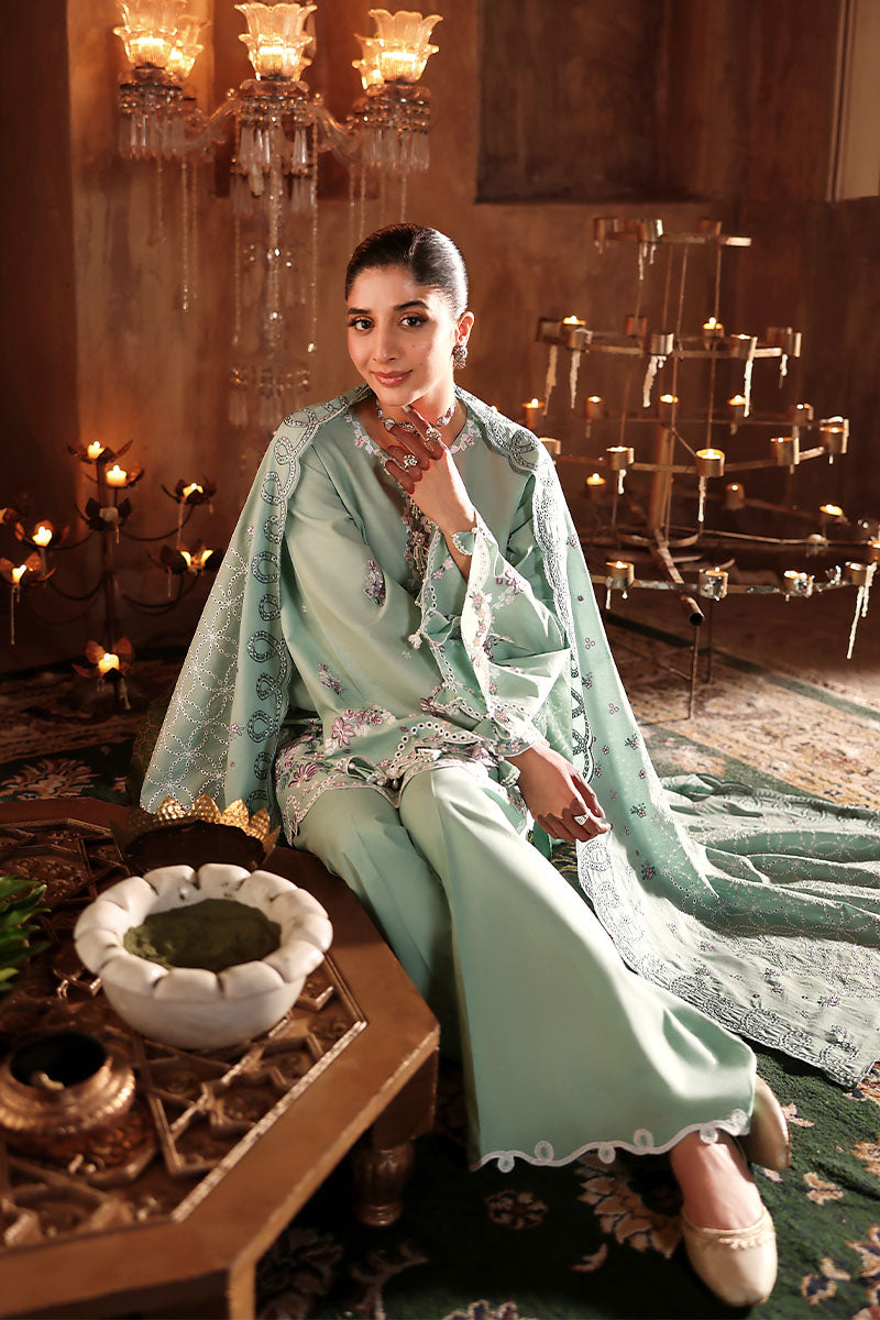 Seated woman dressed in a pastel green embroidered lawn suit, showcasing the detailed embroidery on the dupatta and kameez in a candlelit room.