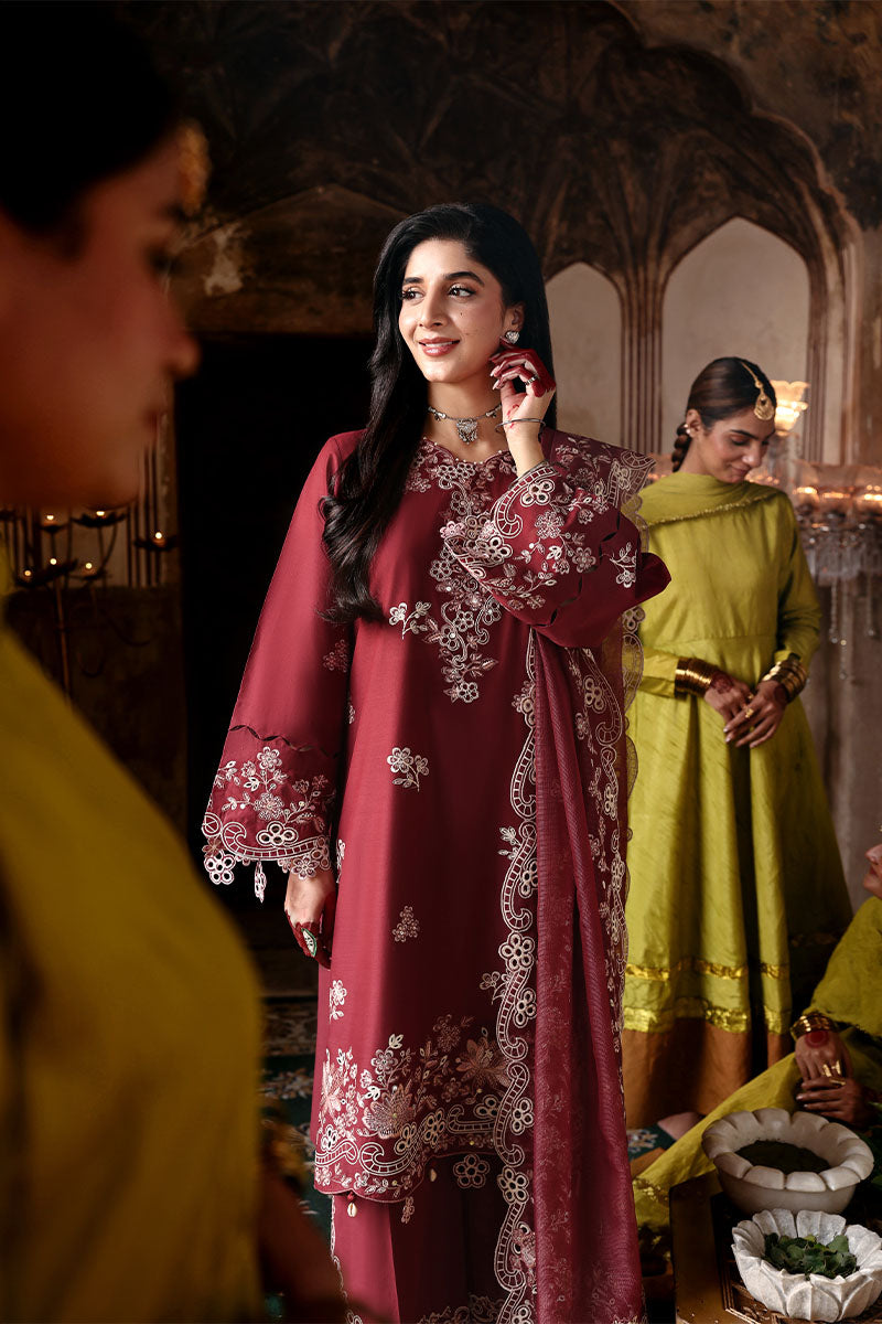Standing woman in embroidered crimson lawn suit showcasing front embroidery and net dupatta with floral details, women in green in background