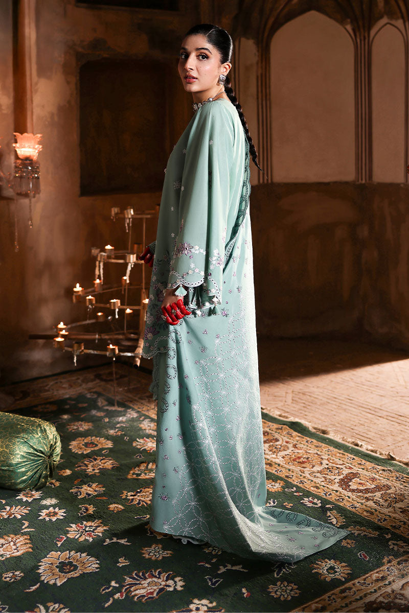 Side profile of a woman in the pastel green embroidered lawn suit featuring scalloped borders and floral embroidery, standing in a warm lit ambiance.