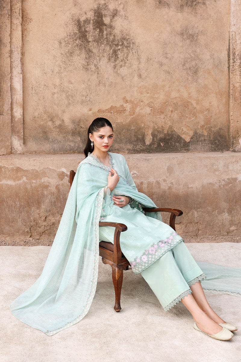 Model seated wearing pastel mint embroidered three-piece suit with flowing dupatta and floral embroidery