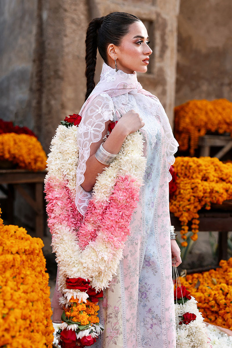 Side profile of a woman wearing the three-piece lawn suit with a floral garland draped over her arm, showcasing the embroidered lace details on the dupatta.