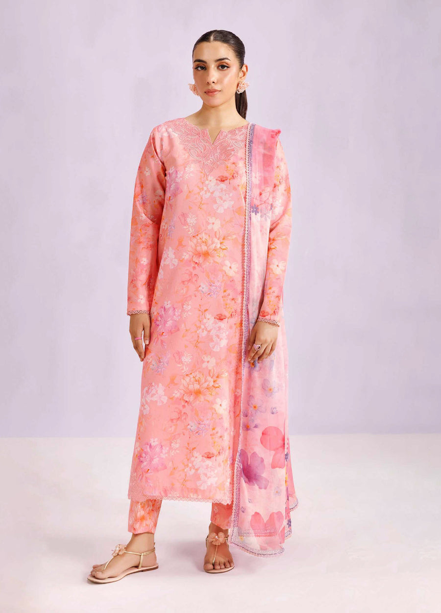 Woman wearing a blush pink floral printed lawn suit with embroidered neckline and matching pants, standing against a neutral background