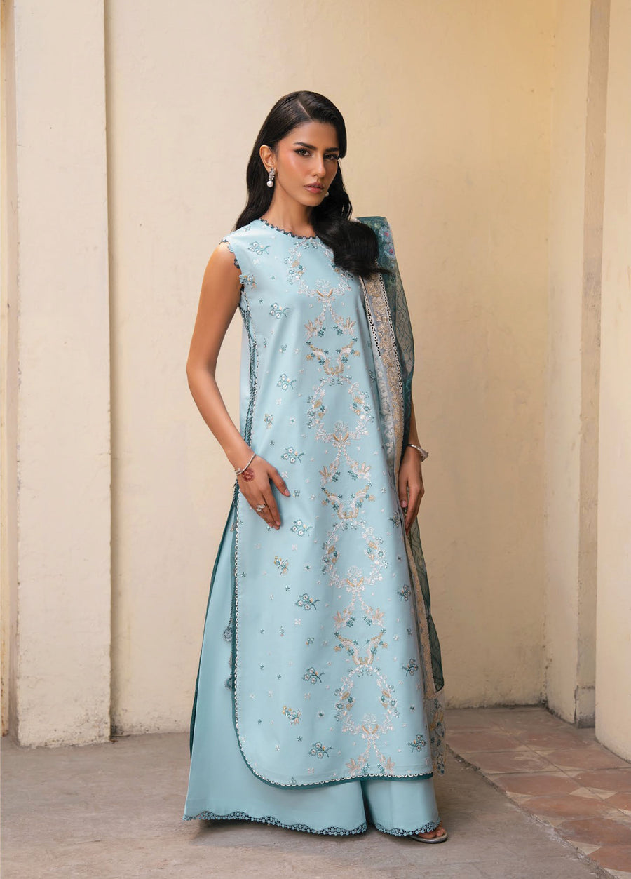 Woman modeling a pastel blue sleeveless embroidered lawn suit with matching wide-legged trousers, standing against a beige wall.
