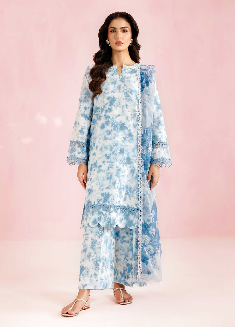 Woman wearing elegant blue and white printed three-piece lawn suit with scalloped lace edges and matching embroidered dupatta, standing against pink background