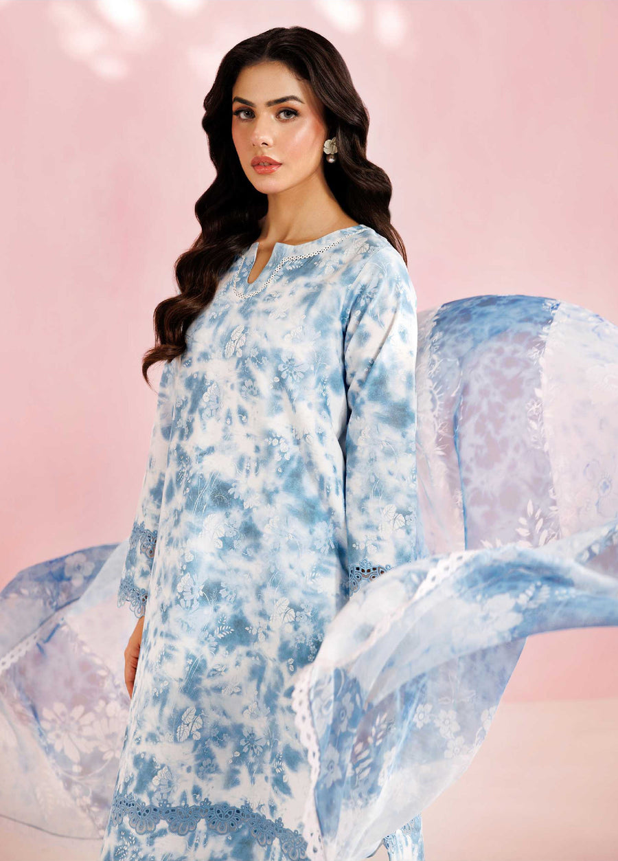 Close-up of woman in blue floral embroidered lawn suit with chiffon dupatta featuring lace border flowing behind her, pink background