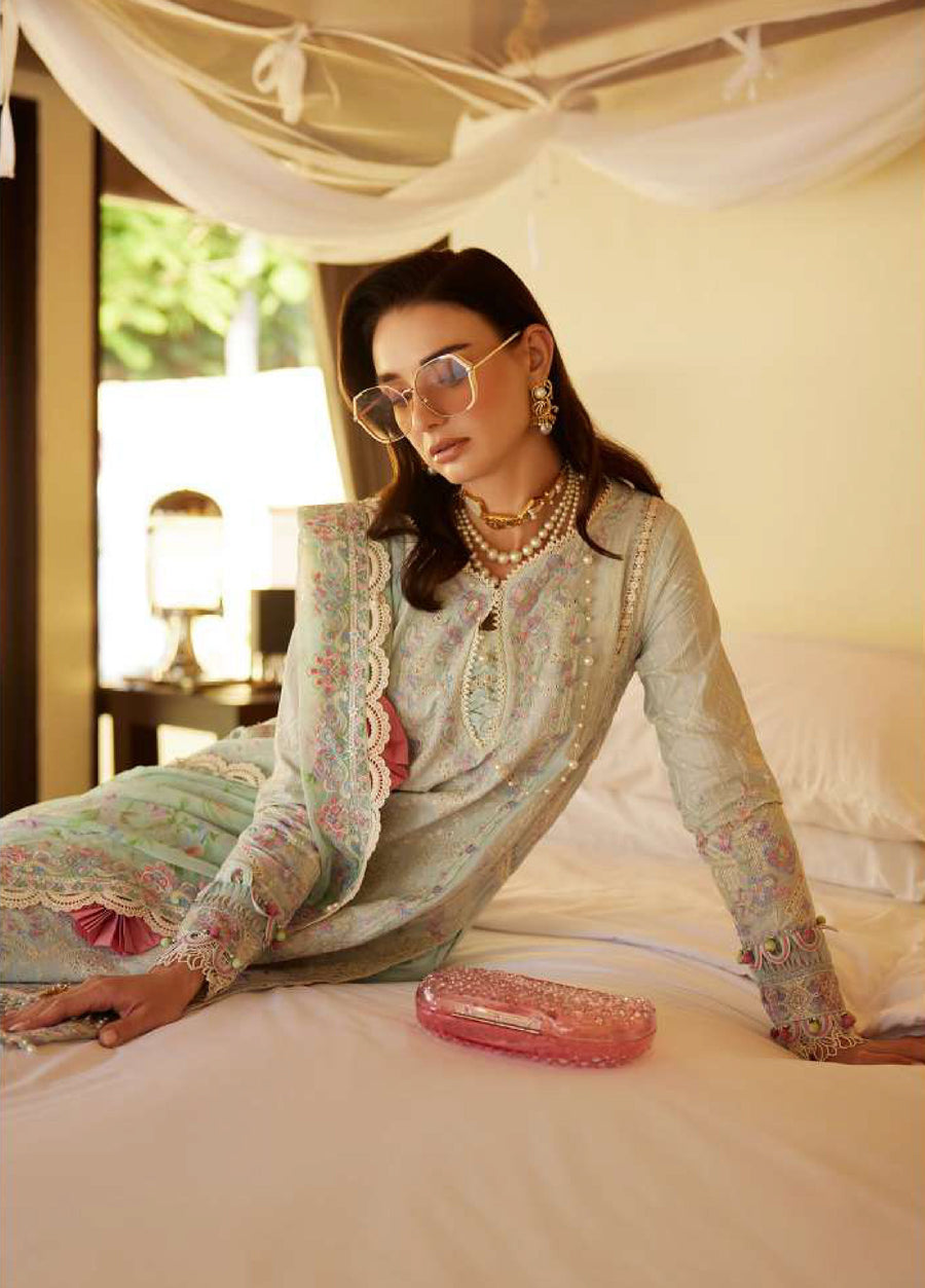Close-up of a woman in an embroidered pastel blue lawn suit with intricate floral embroidery and pearl embellishments resting on a bed beside a pink clutch