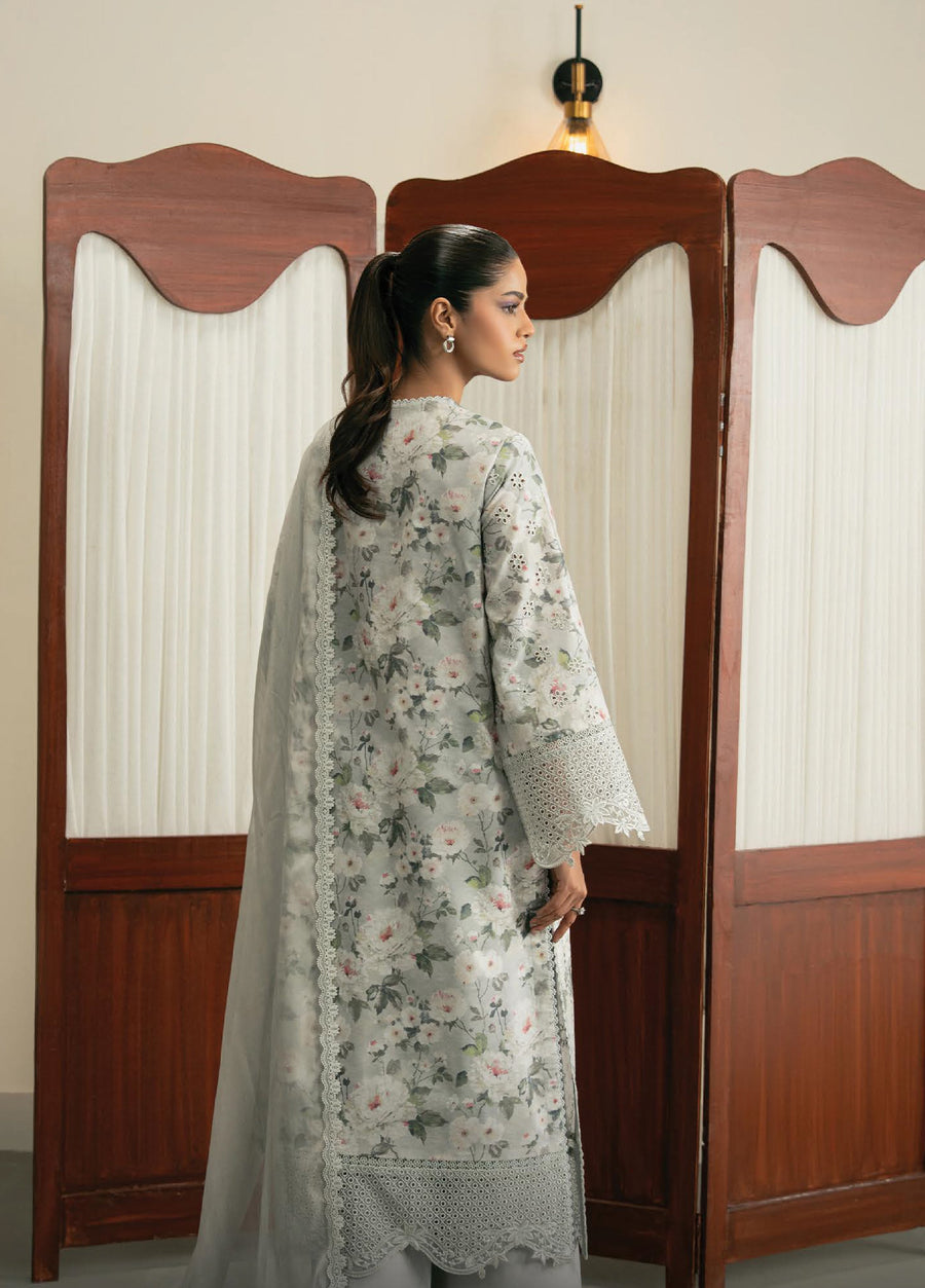 Back view of a woman wearing a light gray floral embroidered suit featuring detailed eyelet lace trims on sleeves and hem, accessorized with a matching plain dupatta, standing against a wooden folding screen.