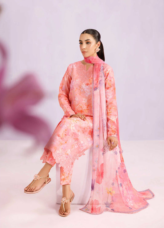Woman seated wearing a blush pink floral printed lawn suit with embroidered neckline and flowing chiffon dupatta, styled for a modest formal look