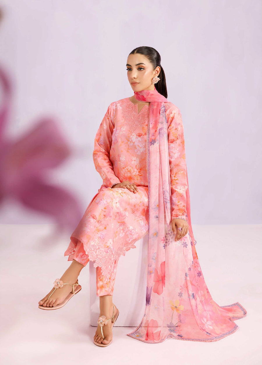 Woman seated wearing a blush pink floral printed lawn suit with embroidered neckline and flowing chiffon dupatta, styled for a modest formal look