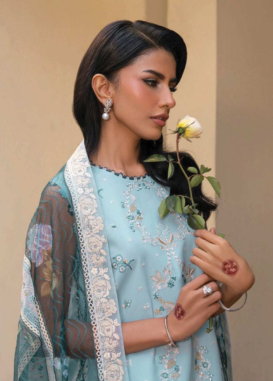 Side profile of woman holding a white rose, highlighting embroidered floral patterns on a pastel blue lawn suit and delicate jewelry accessories.