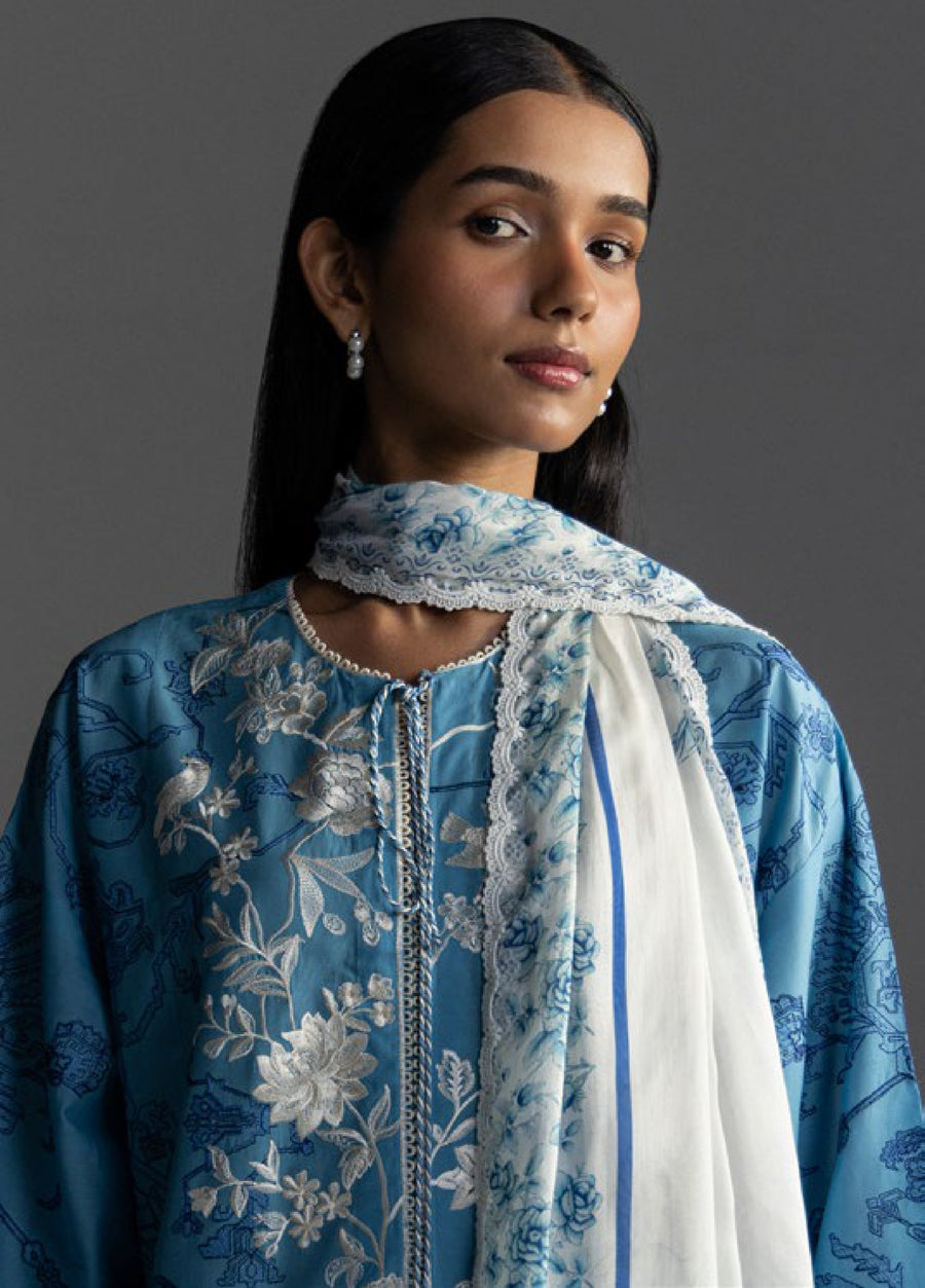 Close-up of woman showing detailed floral embroidery on blue shirt neckline and white floral printed dupatta wrapped around neck