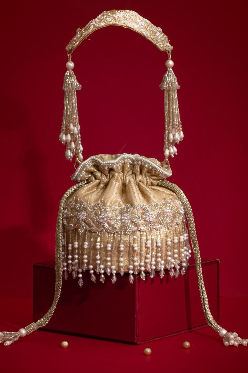 Elegant gold mini potli bag with detailed pearl and bead embroidery and braided handle on red background