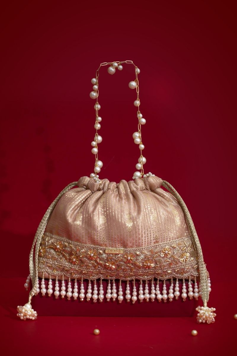 Gold-toned embellished potli bag with pearl bead fringe and decorative chain strap against a red background