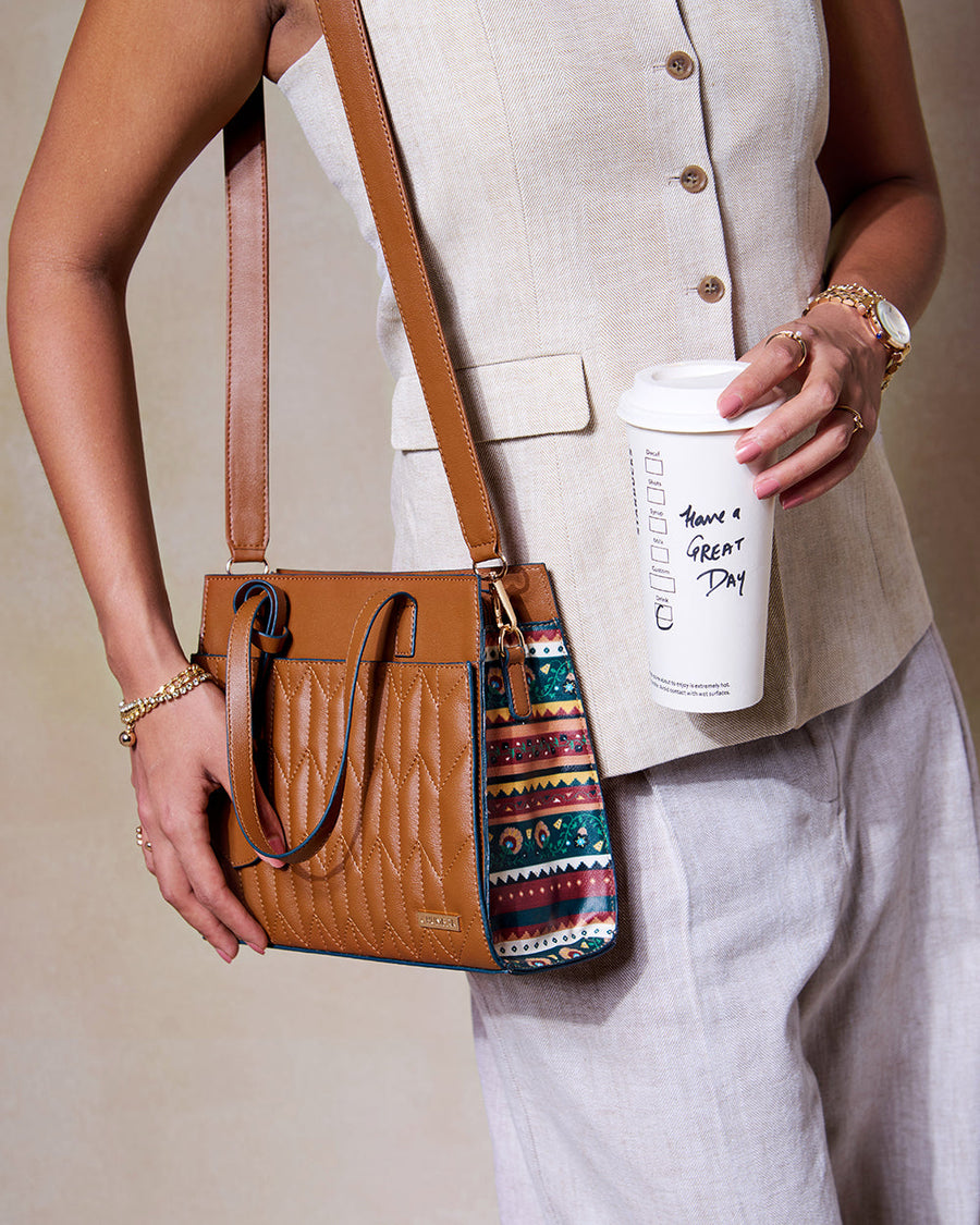 Close-up of woman wearing neutral outfit holding brown quilted handbag with ethnic patterned sides and coffee cup