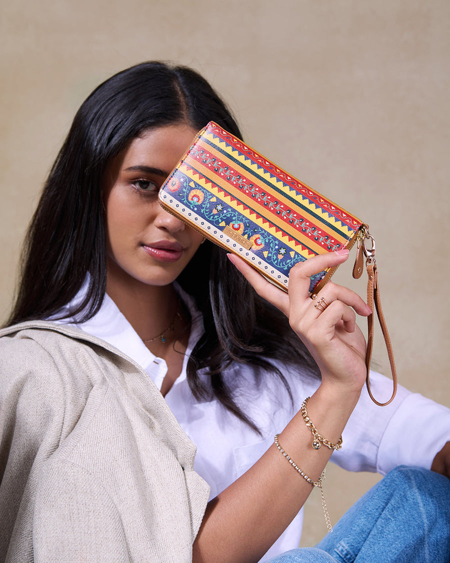 Woman holding a colorful striped and floral patterned wristlet wallet with a leather strap in front of her face