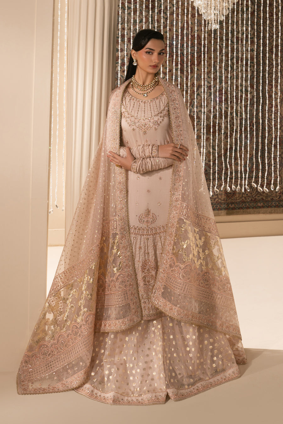 Woman draped in sheer embroidered dupatta over sharara set, showcasing intricate gold floral embroidery and delicate border work