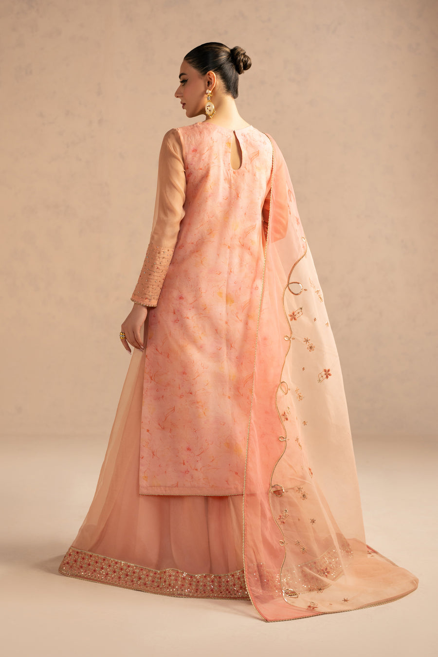 Back view of model in peach organza embroidered suit showing long shirt with slit detail and sharara pants with embellished border