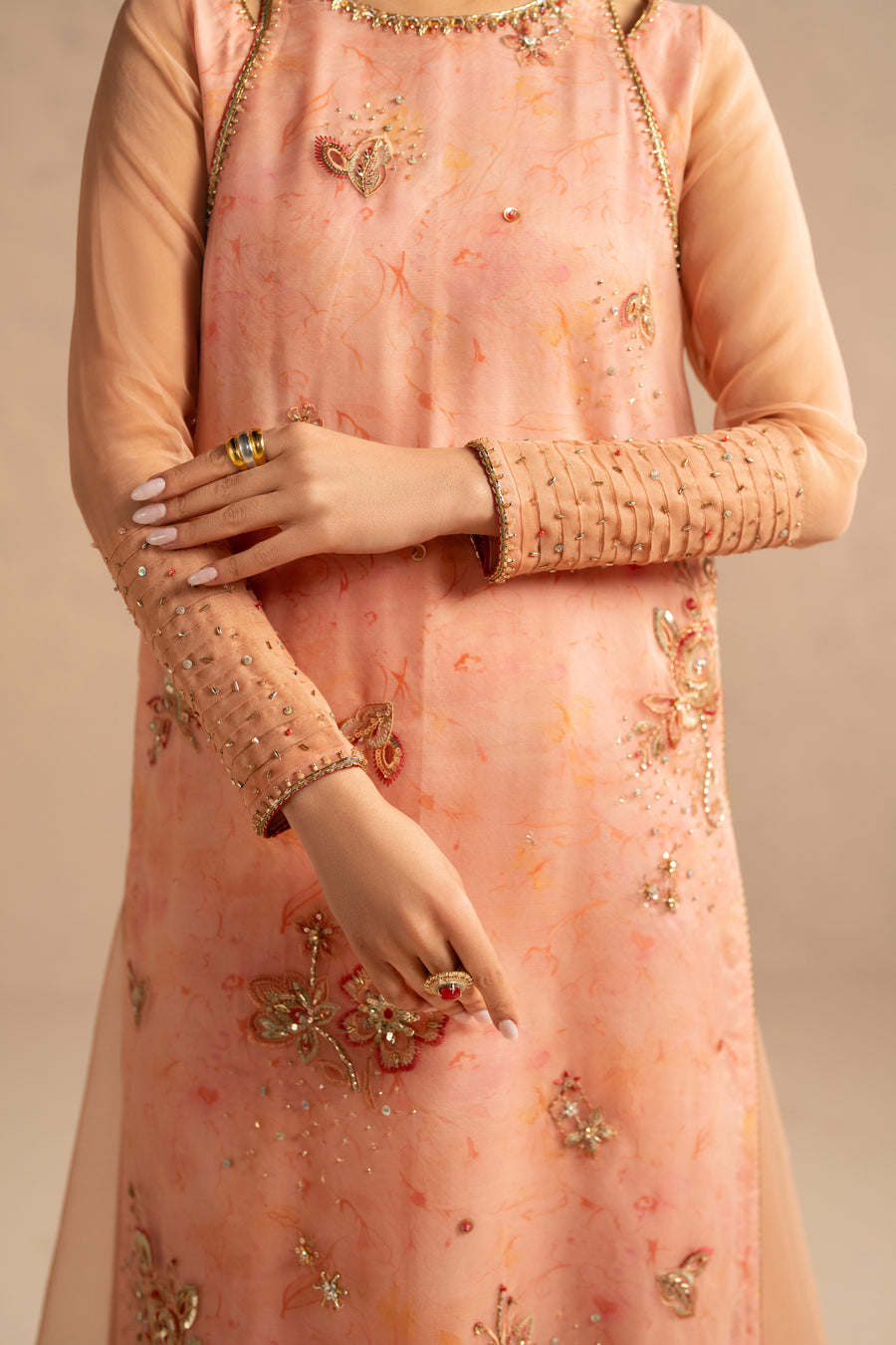 Close-up frontal view of model wearing peach organza shirt with intricate floral embroidery and sequin accents
