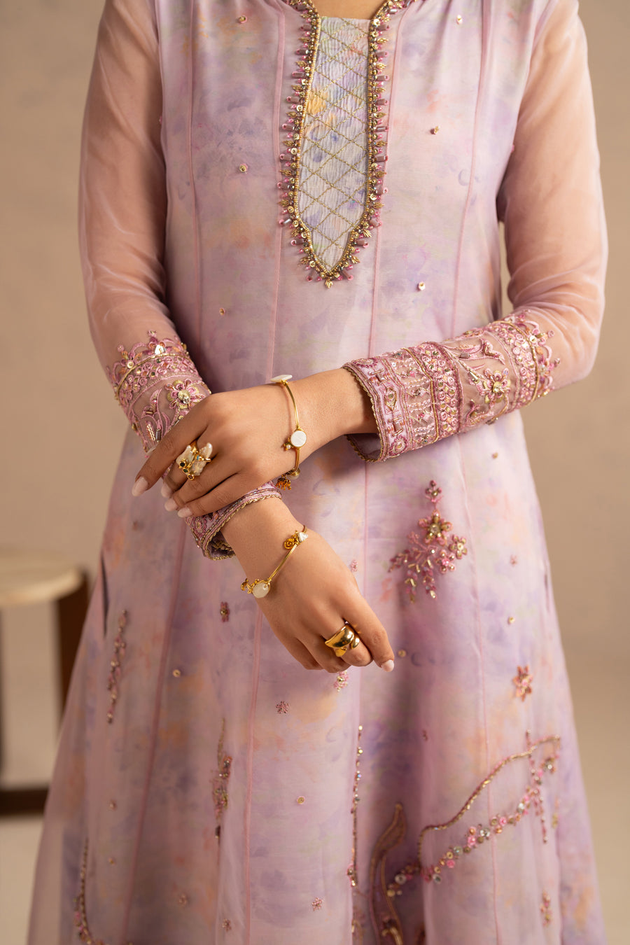 Detailed shot of woman's hands displaying embroidery on frock sleeves and golden jewelry complementing festive look