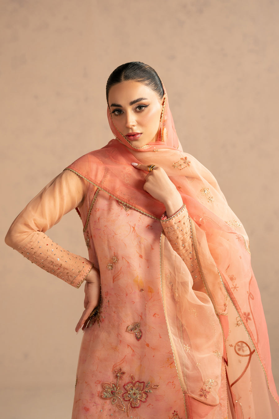 Model posing with sheer peach organza dupatta partially wrapped over head showcasing detailed embroidery and fine finishing