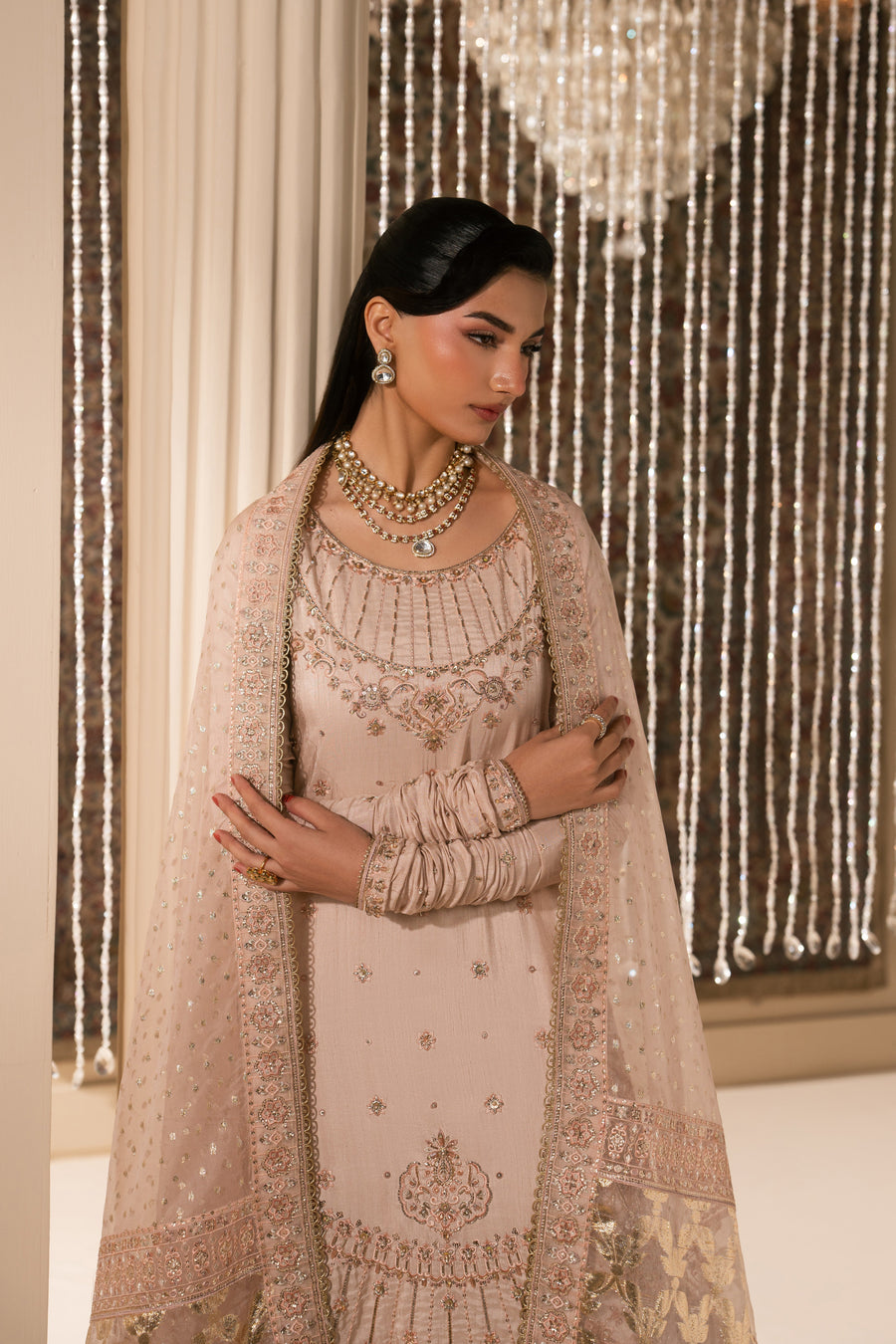 Side angle of woman showcasing embroidered shirt, sheer dupatta, and gold foil sharara pants with elegant jewelry and poised pose