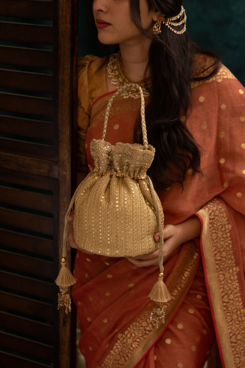 Woman dressed in traditional attire holding an intricately embroidered gold potli bag with drawstring tassels and braided handle
