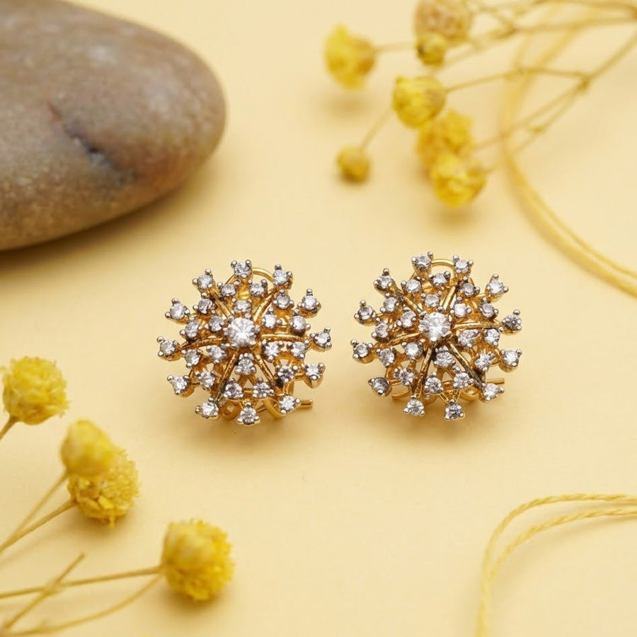 Gold and crystal starburst earrings placed on yellow background with decorative dried flowers