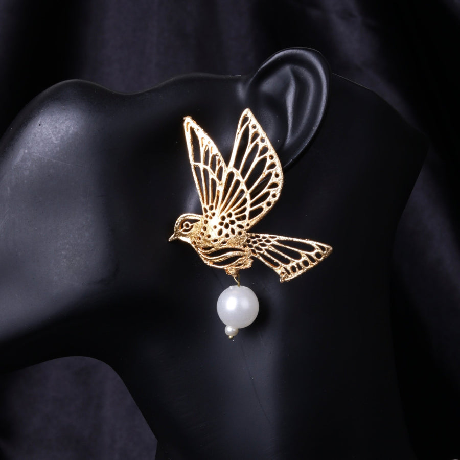 Close-up of gold bird-shaped earring with a dangling white pearl on black mannequin ear