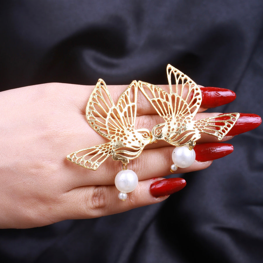 Gold bird pearl earrings showcased on a hand with red nail polish against a black fabric background