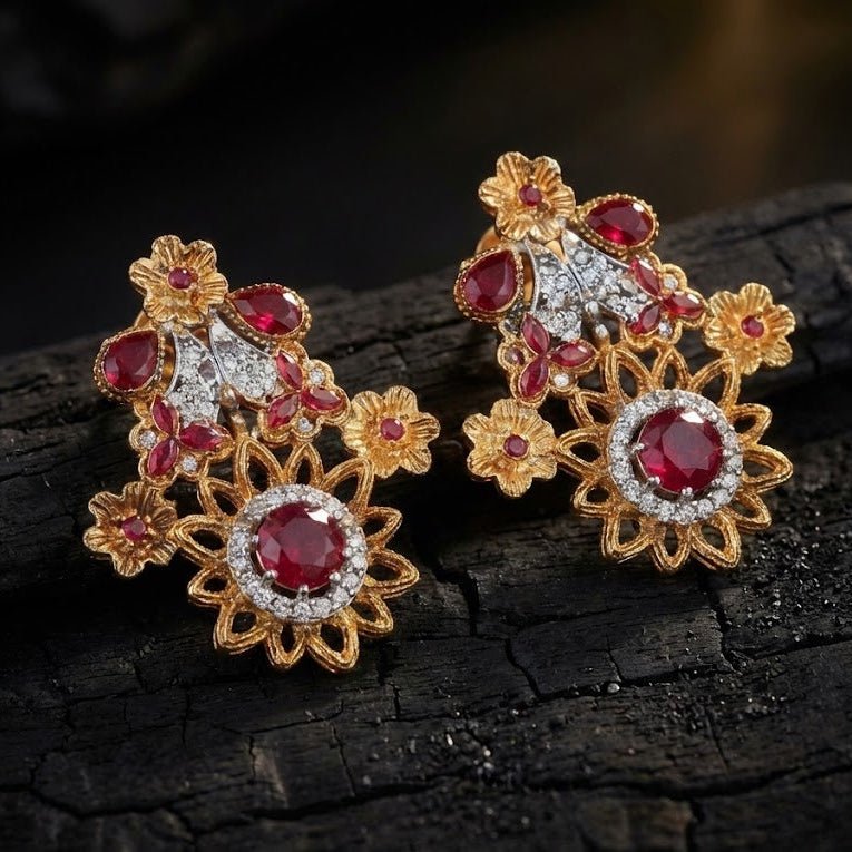 Floral red gemstone earrings with intricate gold-tone metal detailing positioned on dark textured surface