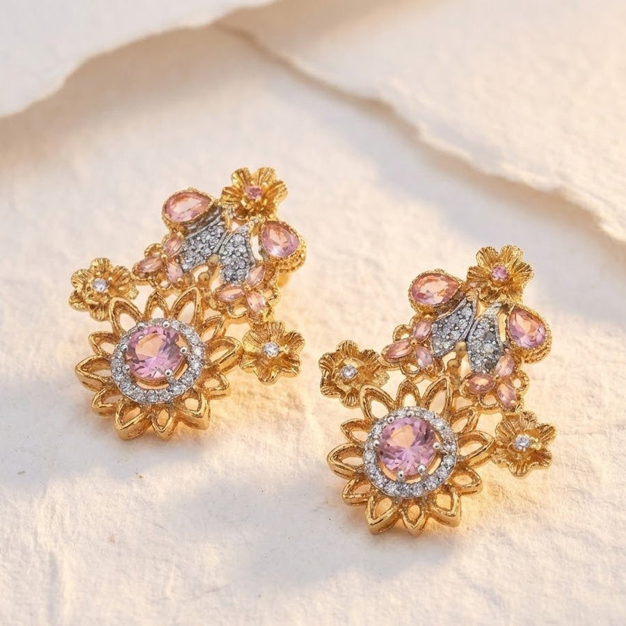 Close-up of floral earrings with dark deep blue gemstones and sparkling clear accents set in polished gold-tone metal