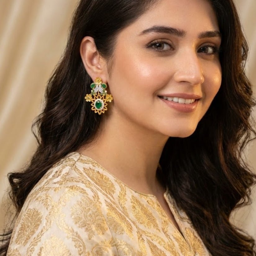 Woman wearing green floral gemstone statement earrings with cream and gold traditional attire smiling indoors