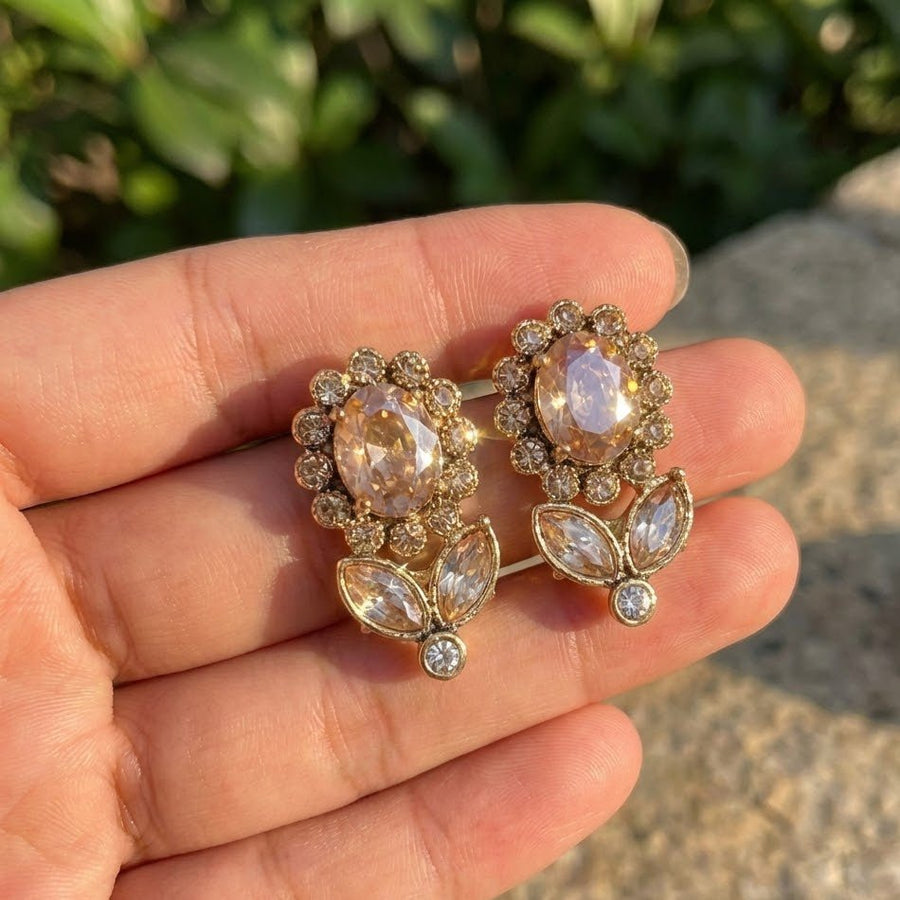 Hand holding a pair of gold-tone floral earrings showcasing their size and sparkle under sunlight