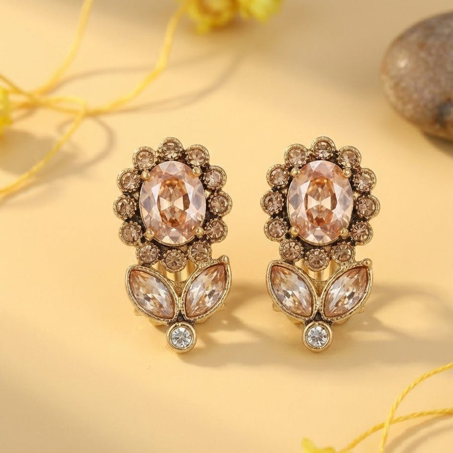 Gold-tone floral earrings displayed against soft yellow background with decorative stones and flowers