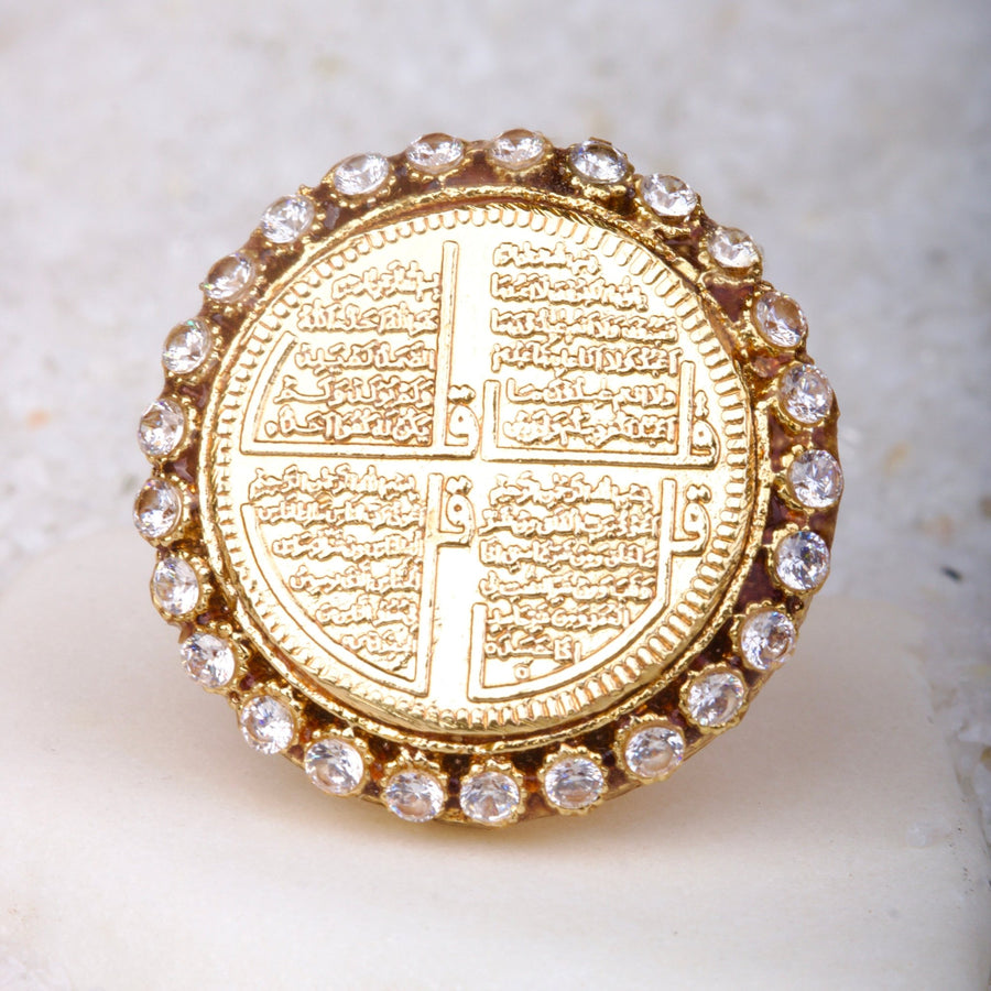 Close macro image of gold coin ring with intricate Surah engravings and surrounding sparkling clear stones on light surface