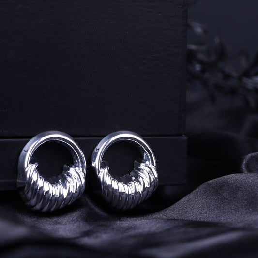 Silver sculpted textured hoop earrings with ribbed detailing on a black fabric background