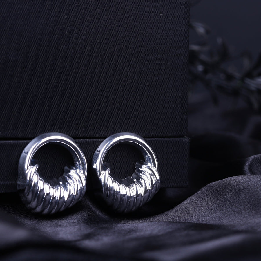 Silver sculpted textured hoop earrings with ribbed detailing on a black fabric background