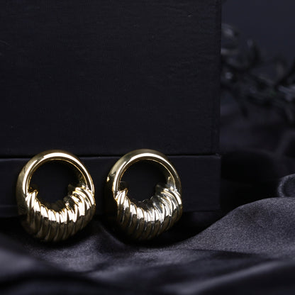 Gold sculpted textured hoop earrings with ribbed detailing on a black fabric background