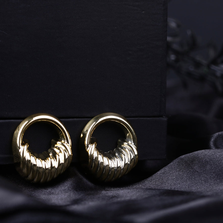 Gold sculpted textured hoop earrings with ribbed detailing on a black fabric background