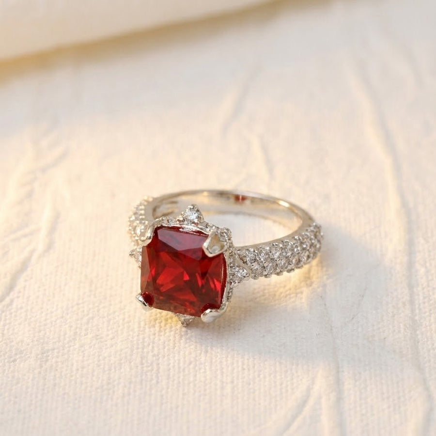 Silver cocktail ring with deep red cushion-cut gemstone placed on white textured fabric