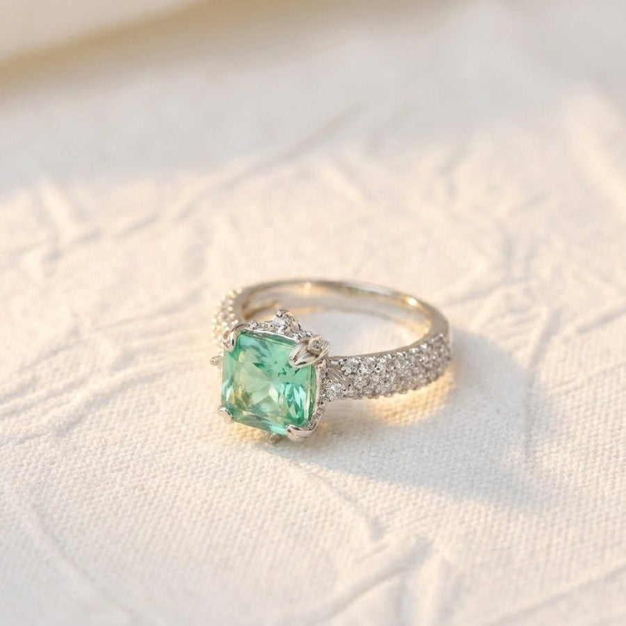 Silver cocktail ring with light green cushion-cut gemstone placed on white textured fabric