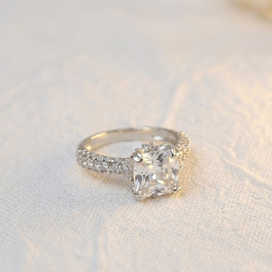Silver cocktail ring with clear white cushion-cut gemstone placed on white textured fabric