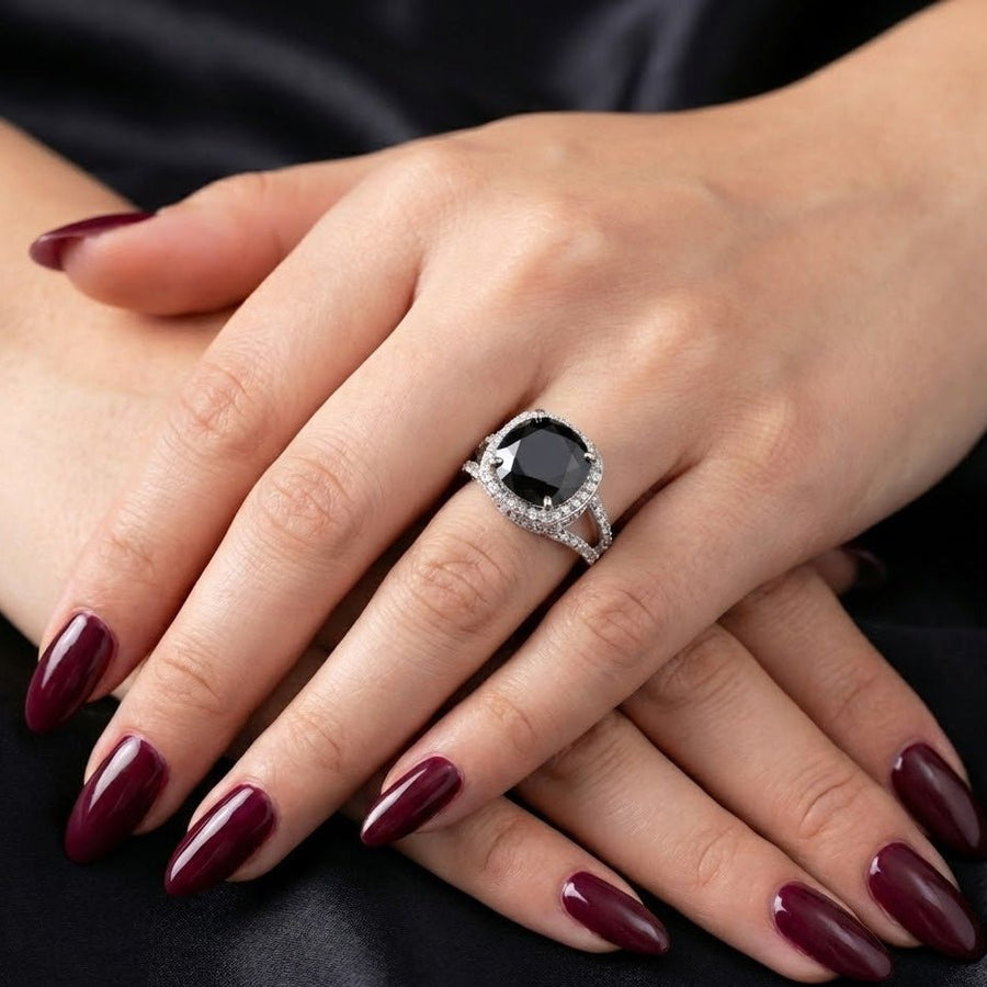 Women's hand showing cushion-cut black gemstone pavé ring with dark red manicure
