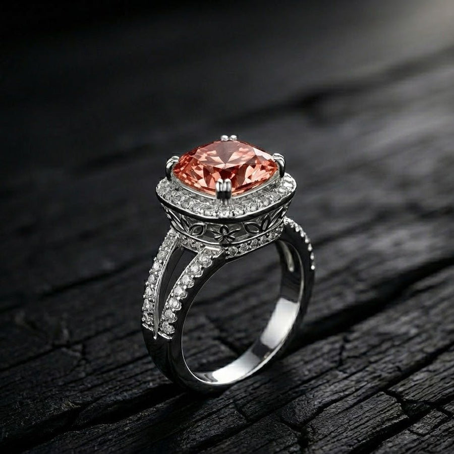 Close-up of cushion-cut peach gemstone ring with double pavé halo and floral engravings on dark textured surface